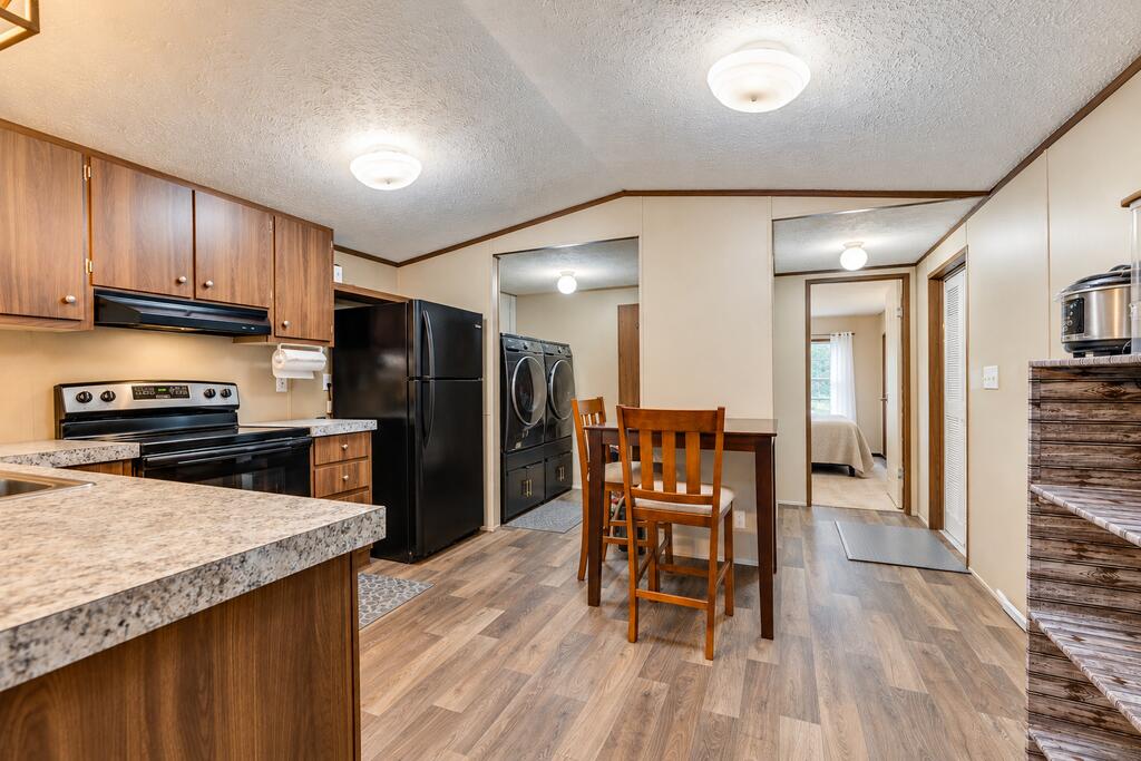 Kitchen and dining area with wood cabinets, black appliances, and laundry machines beside the table.