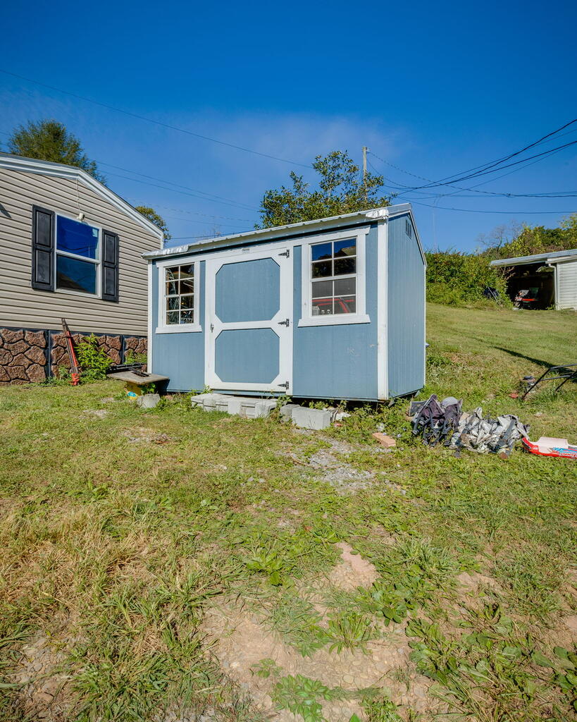 Light blue storage shed beside a manufactured home, with debris scattered across the grassy yard.