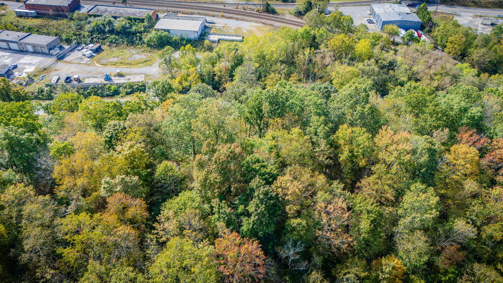 Aerial view of a wooded property with autumn foliage, nearby buildings, and railroad tracks.
