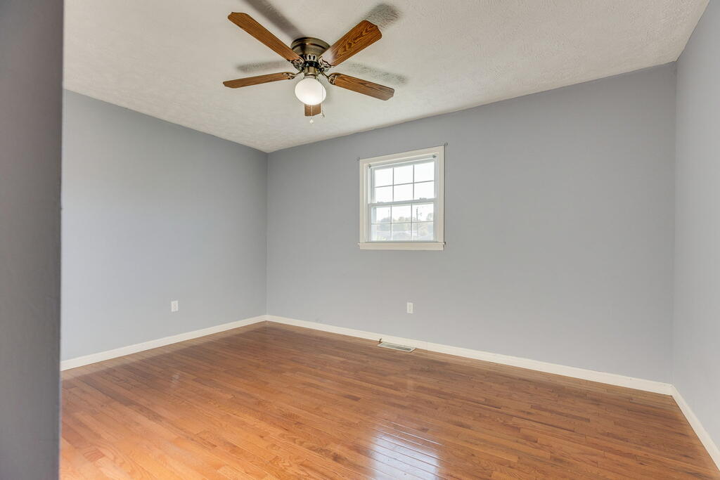 Empty room with gray walls, hardwood floors, a small window, and a ceiling fan.