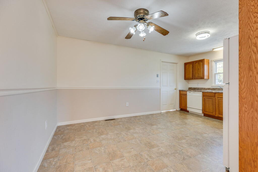 Empty dining area with beige tile and a compact kitchen with wood cabinets and a white dishwasher.