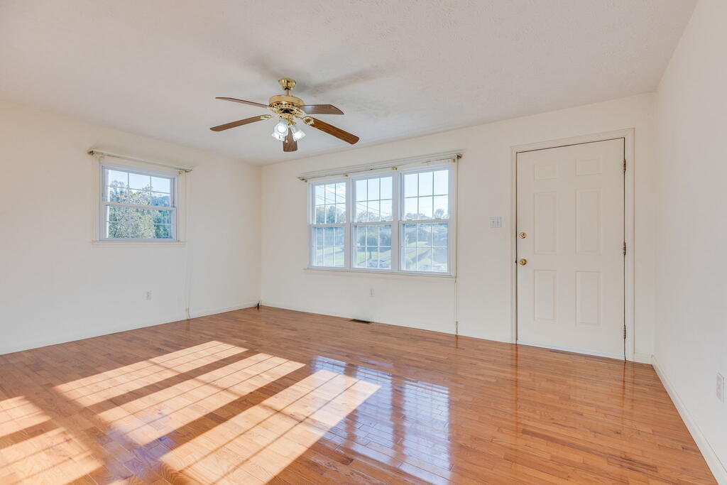 Vacant room with glossy hardwood floors, two windows, and a ceiling fan.