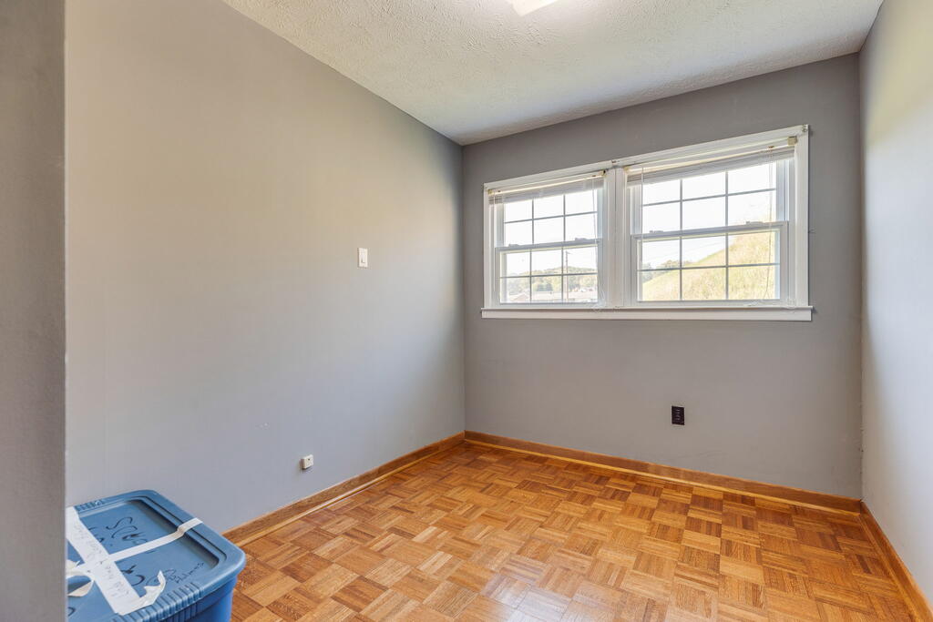 Empty room with parquet flooring and two side-by-side windows.