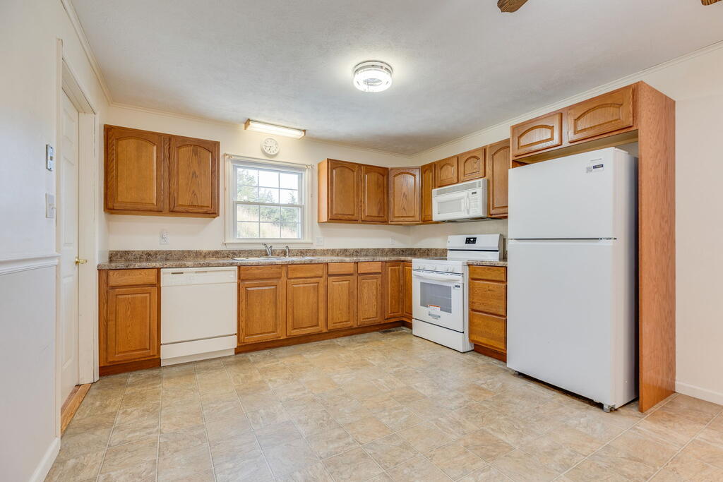 Kitchen with honey-colored wood cabinets, white appliances, tiled floors, and a window above the sink.