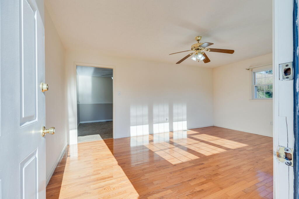 Empty room with polished hardwood floors, a ceiling fan, and sunlight streaming through the window.