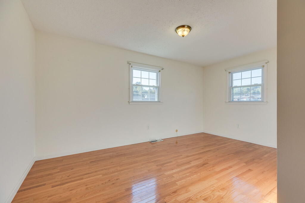 Empty room with polished hardwood floors and two windows.