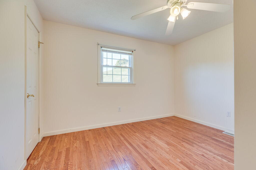 Vacant bedroom with hardwood floors, a ceiling fan, and a single window.