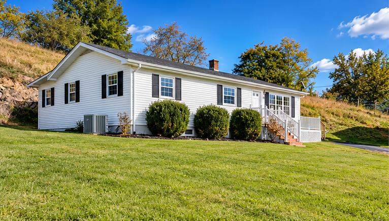 White single-story house with dark shutters, front steps, and trimmed shrubs beside a broad lawn.
