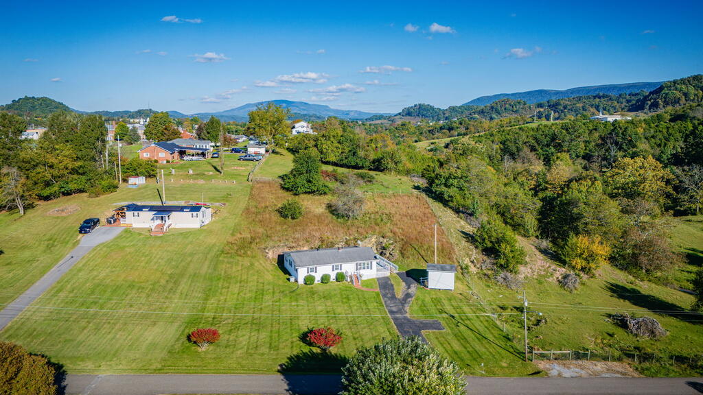Aerial view of a home and outbuilding on a broad lawn, with wooded hills and distant mountains.