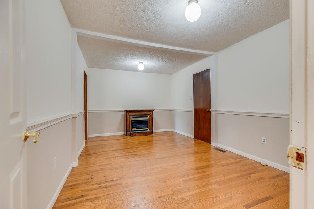 Empty living room with hardwood floors, chair rail molding, and a small fireplace with a wood mantel.
