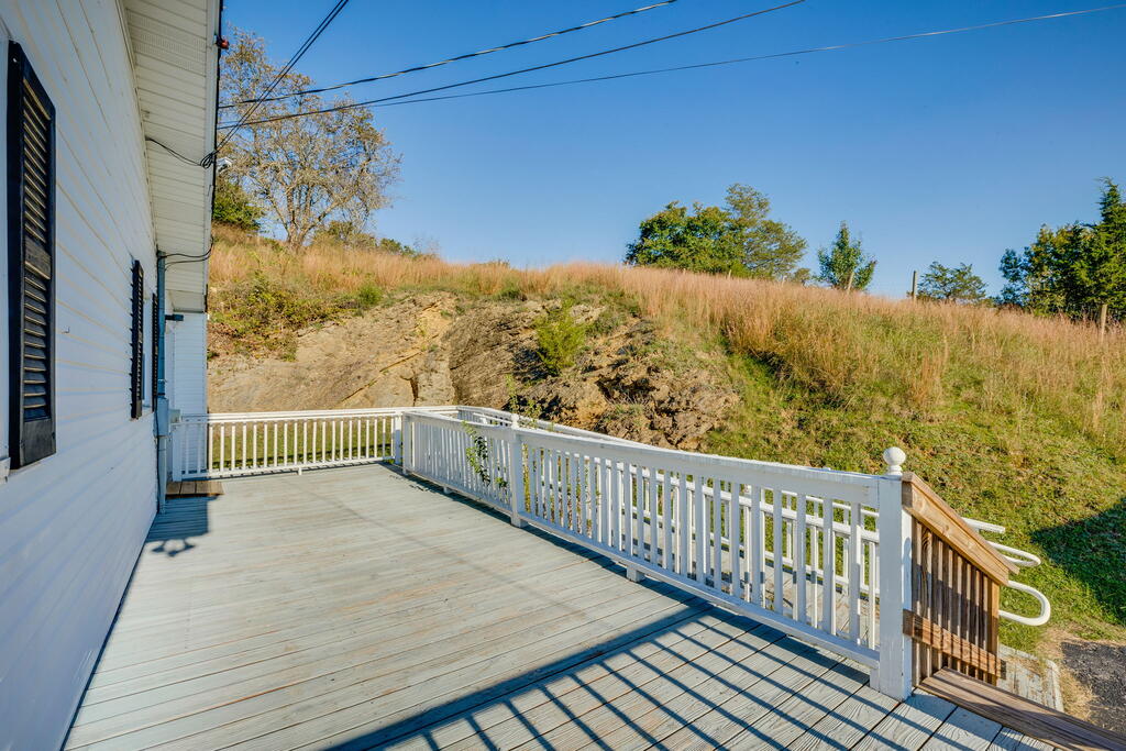 Wooden deck with white railings beside a white-sided house, overlooking a grassy hillside.