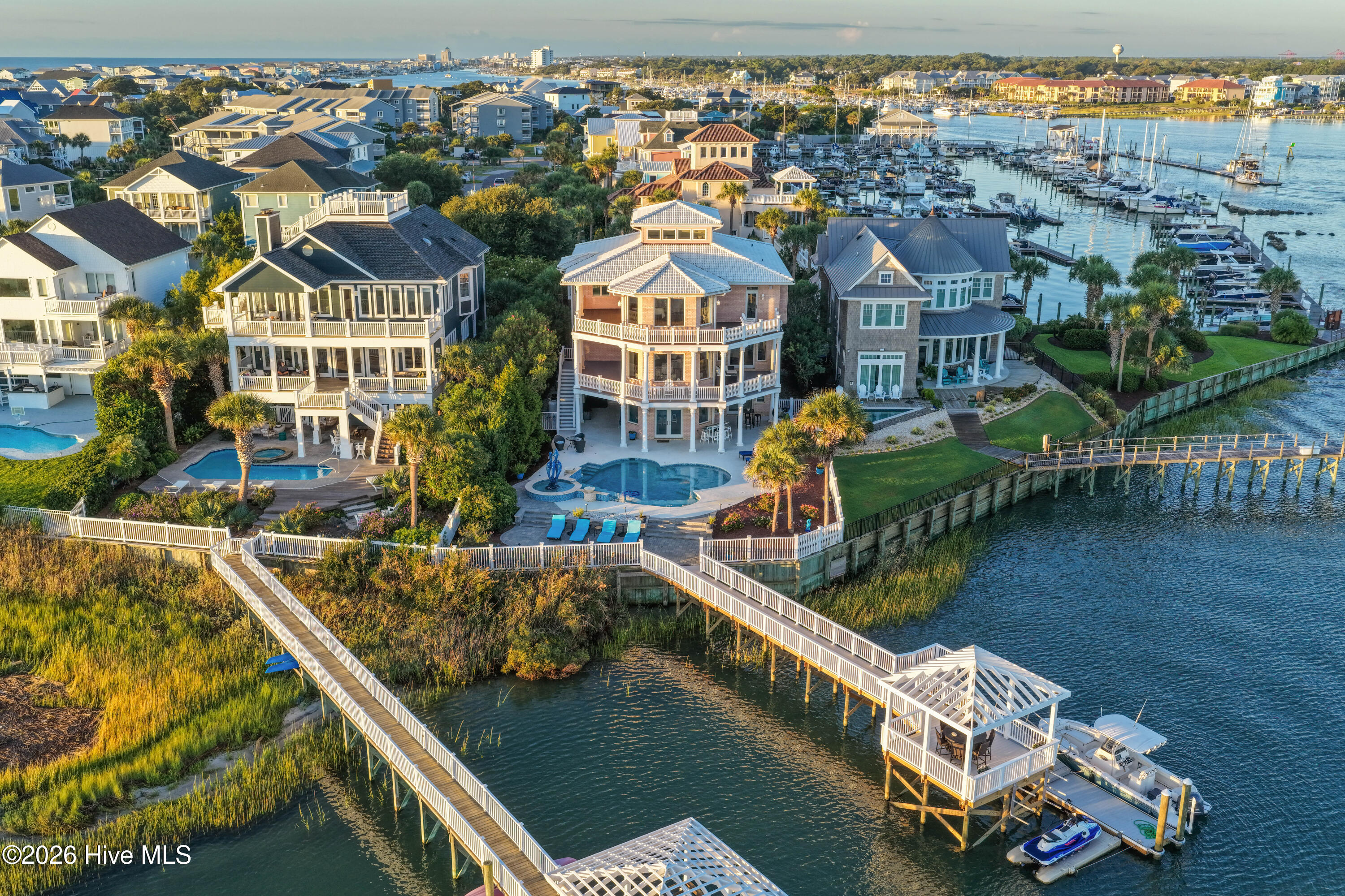 Aerial view of a waterfront home with a pool, boardwalk, covered dock, and marina beyond.