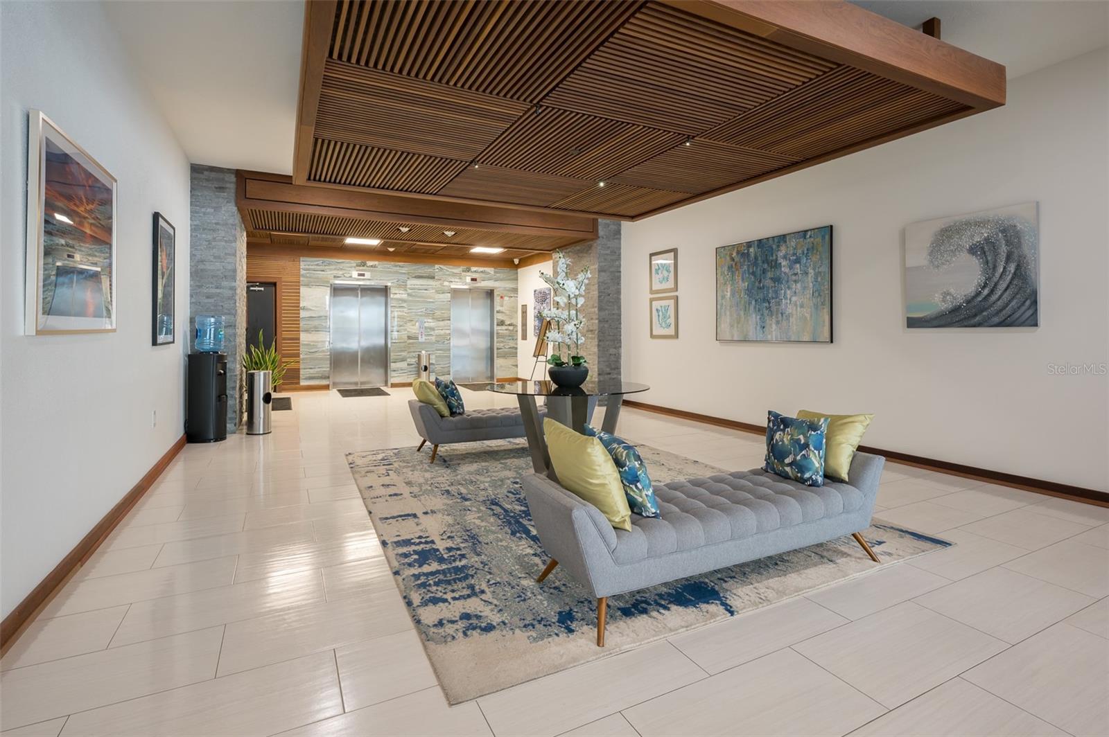 Condominium lobby with two elevators, gray sofas, and a prominent wood-slat ceiling.