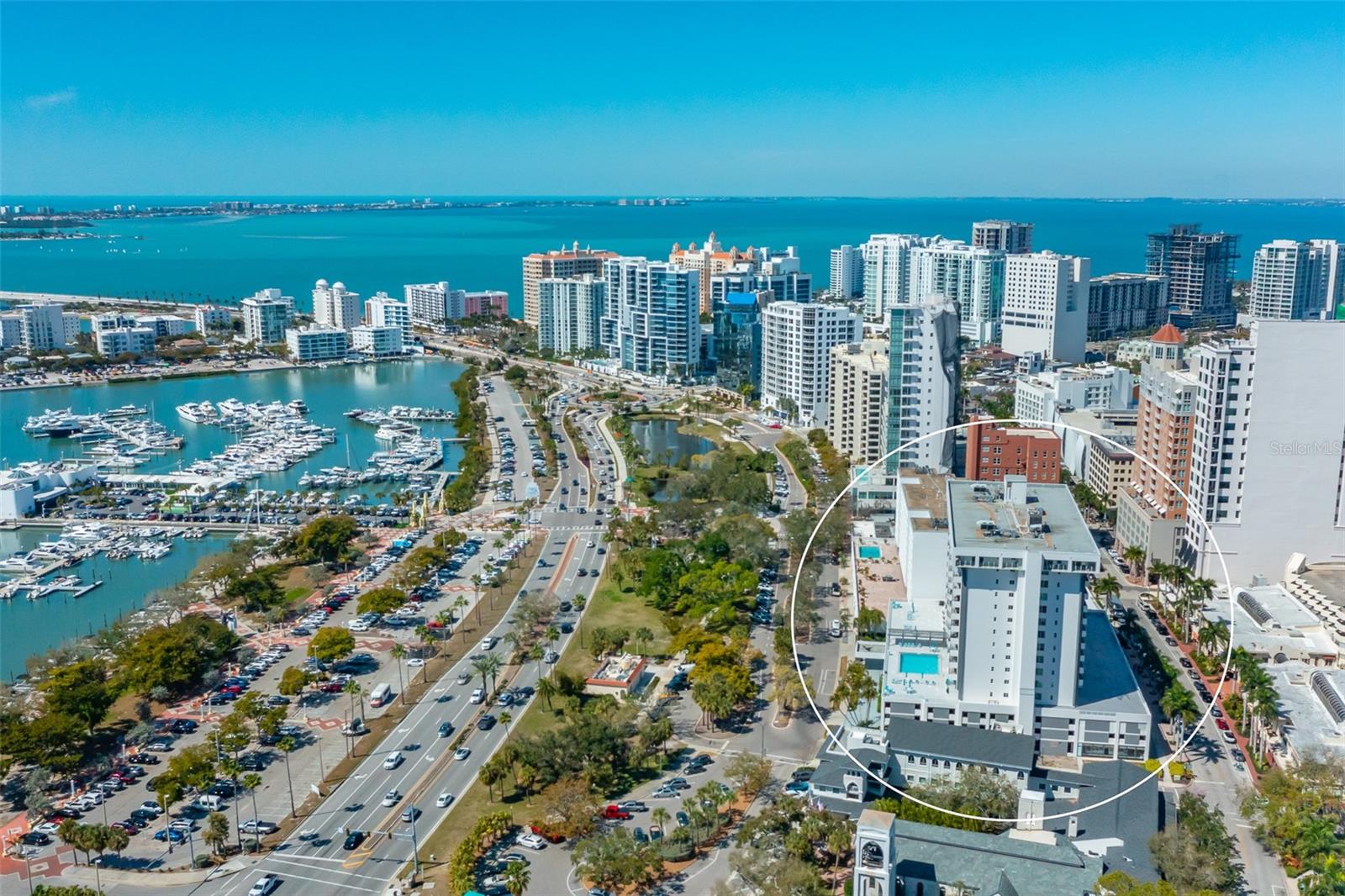 Aerial view of a Sarasota waterfront condominium highlighted among downtown towers, marina, and blue bay.