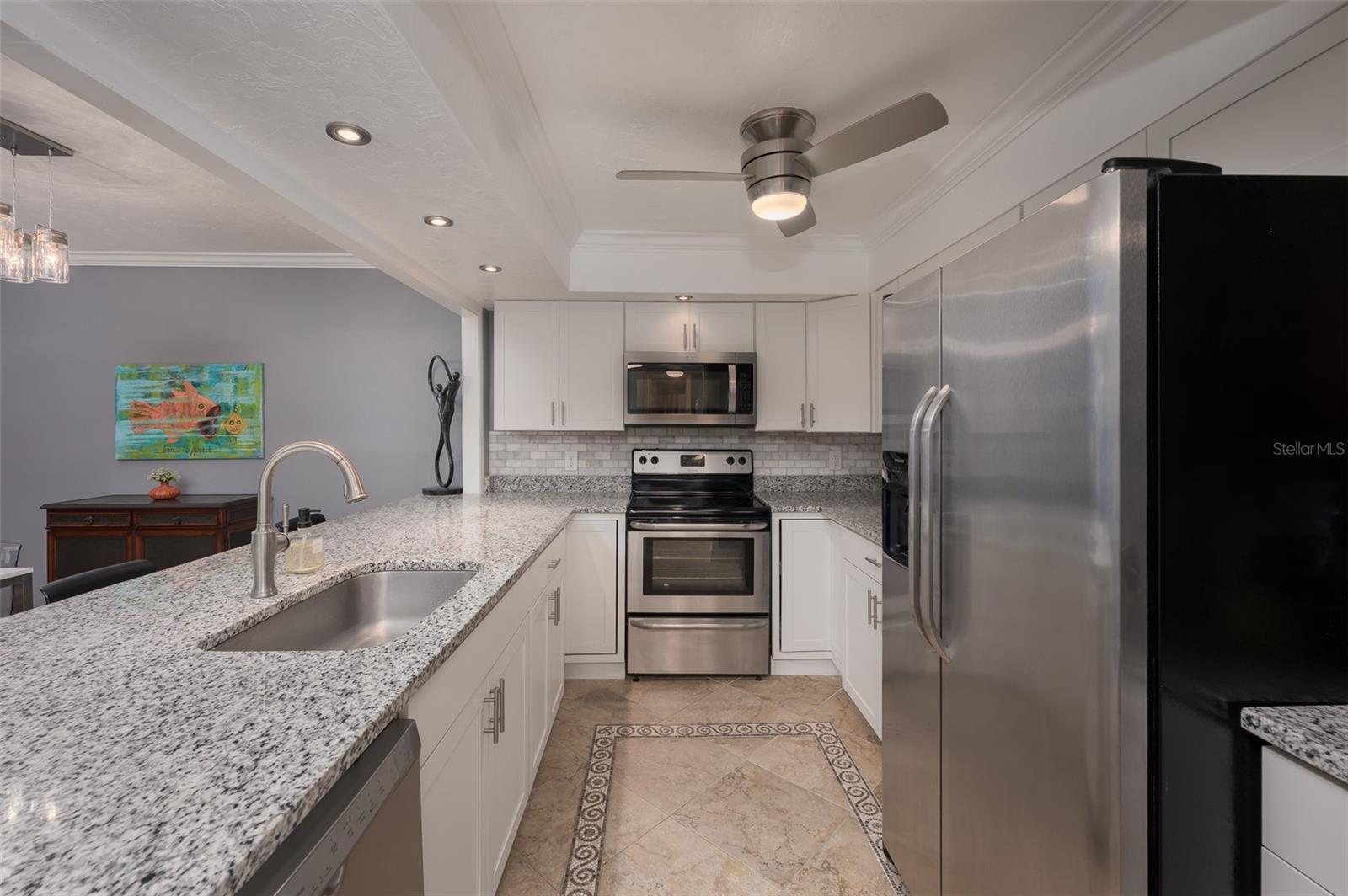 Condo kitchen with white cabinets, granite counters, stainless steel appliances, and a large island sink.