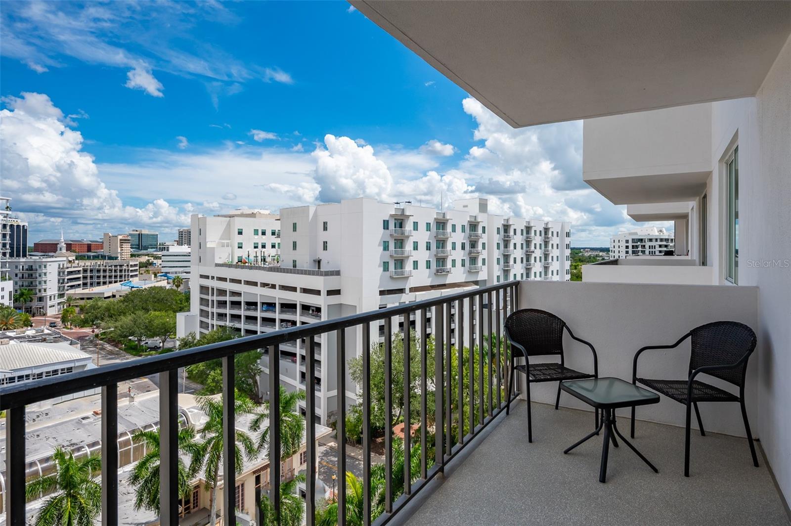 High-rise balcony with black chairs overlooking downtown buildings and palm trees.