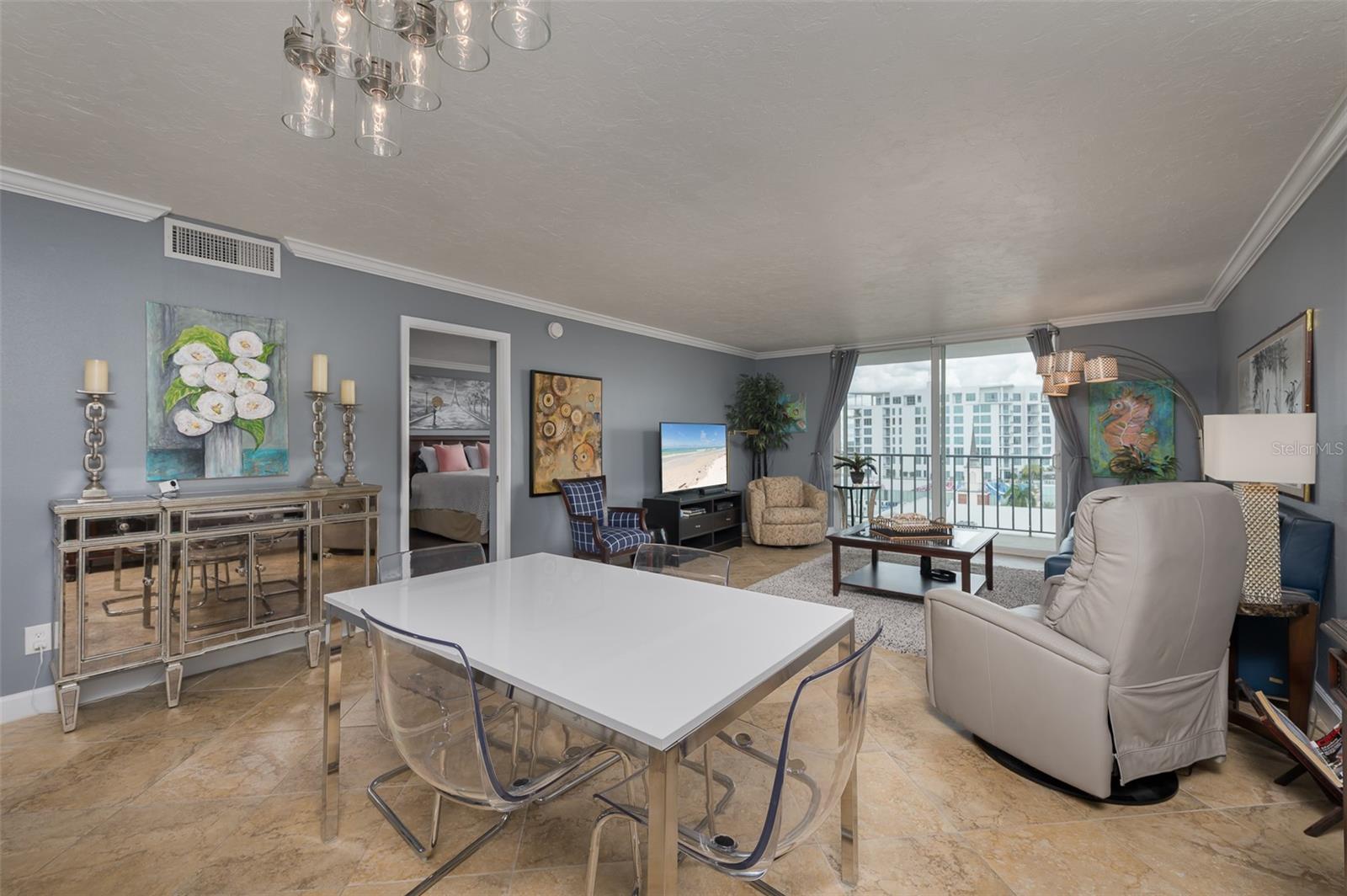 Condominium living and dining room with marble floors, a white table, and sliding doors overlooking neighboring buildings.