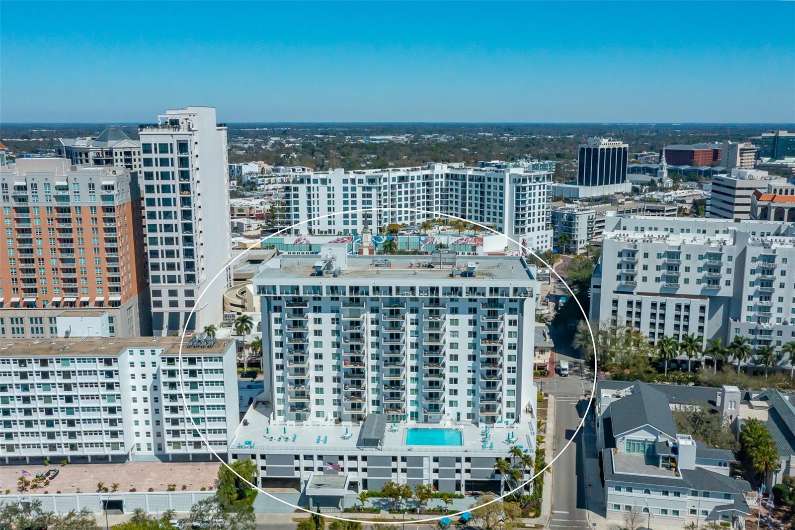 Aerial view of a Sarasota condominium tower with balconies and a rooftop pool, outlined in white.