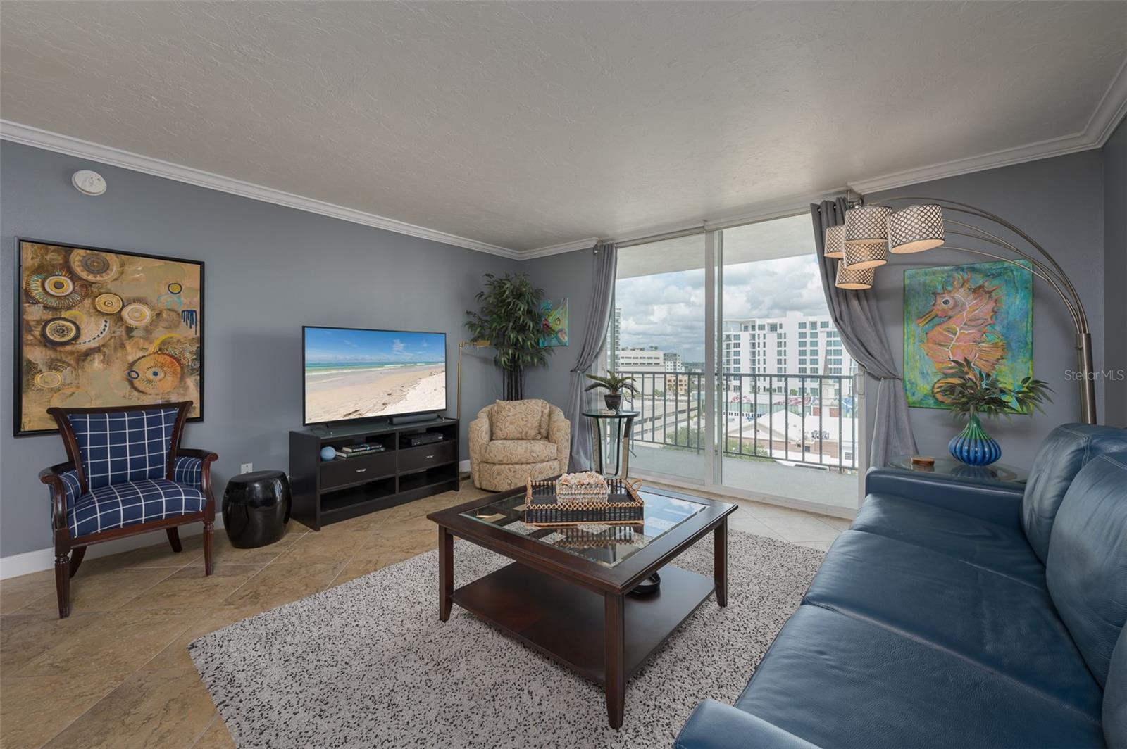 Condominium living room with blue sofa and balcony doors overlooking nearby city buildings.