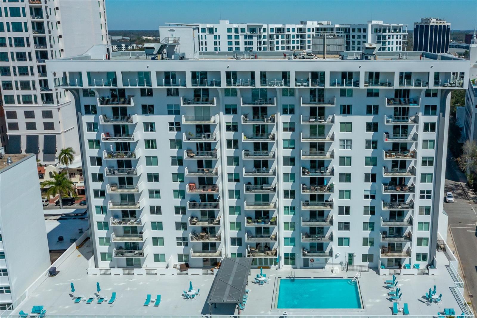 White condominium building with rows of balconies overlooking a swimming pool deck.