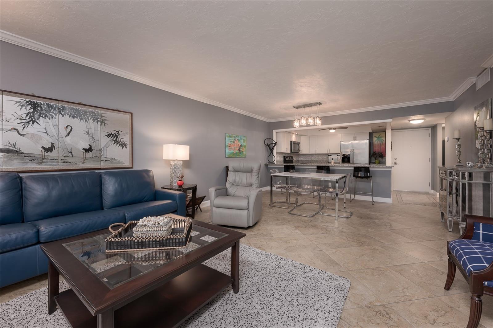 Furnished condo living room with blue sofa, dining table, and open kitchen.