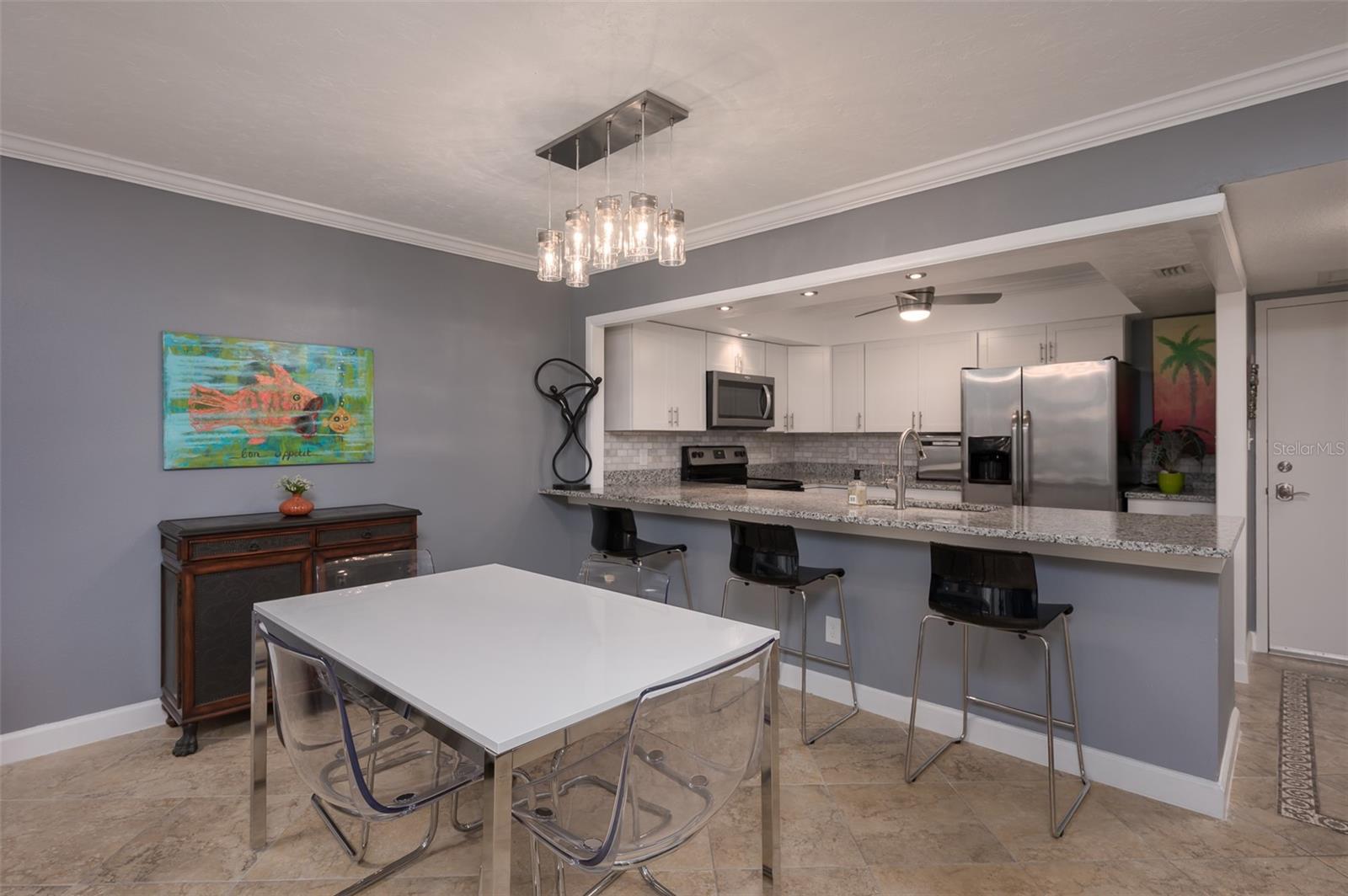 Condo dining area and open kitchen with a white table, breakfast bar, and stainless steel appliances.