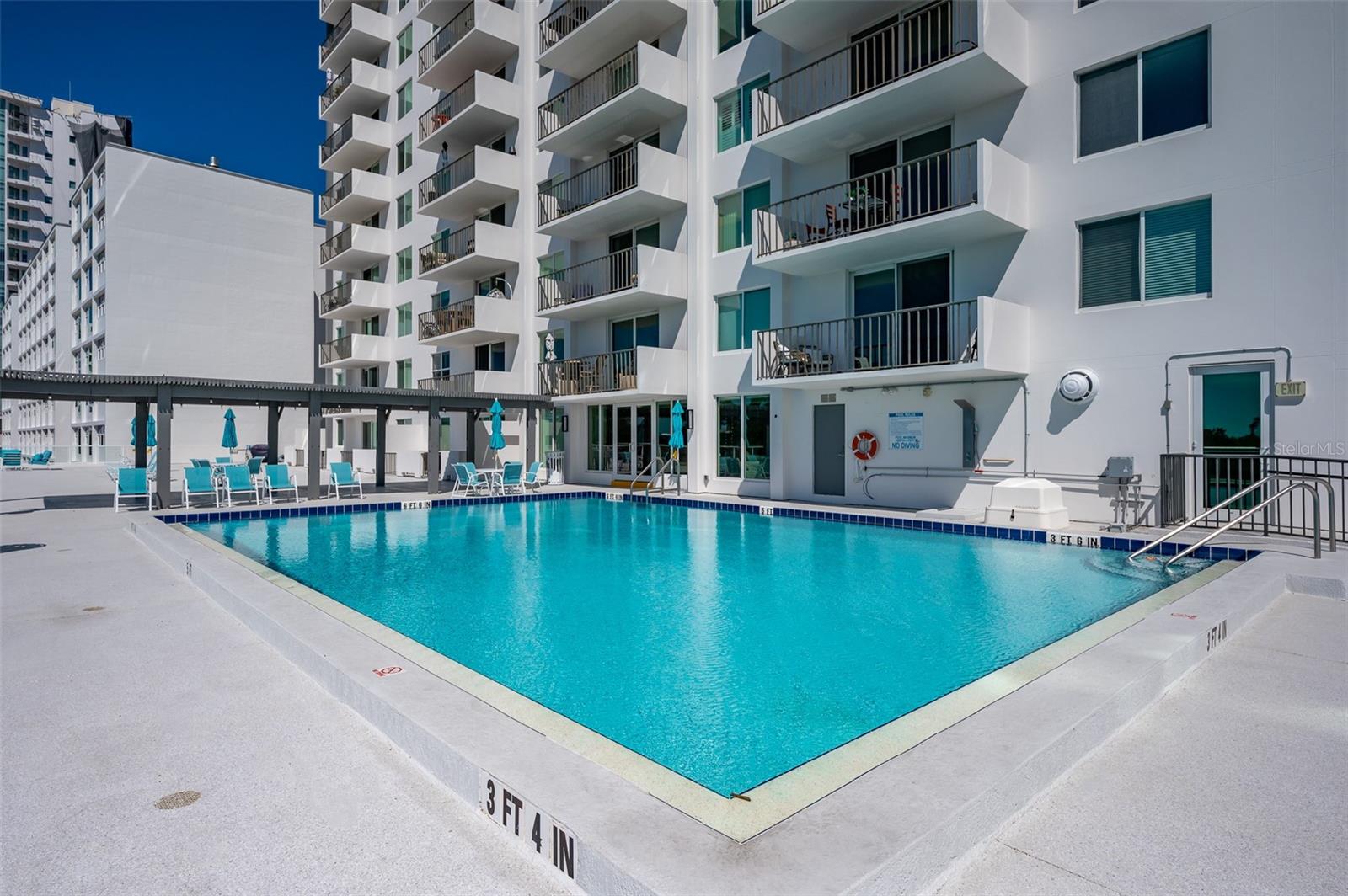 Condominium swimming pool with turquoise water, blue umbrellas, and white balconies surrounding the deck.