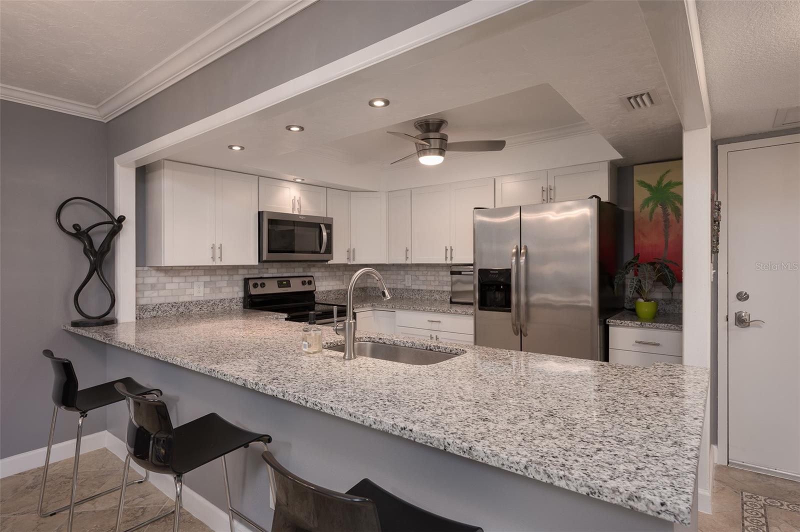 Kitchen with a long granite breakfast bar, white cabinets, and stainless steel appliances.
