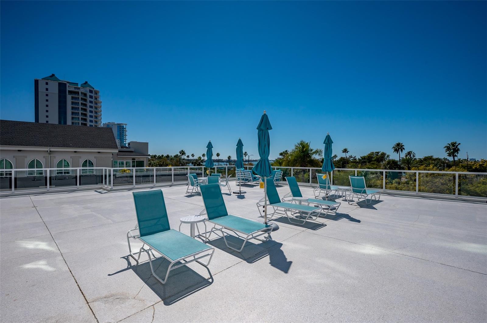 Rooftop terrace with turquoise loungers and umbrellas overlooking water.
