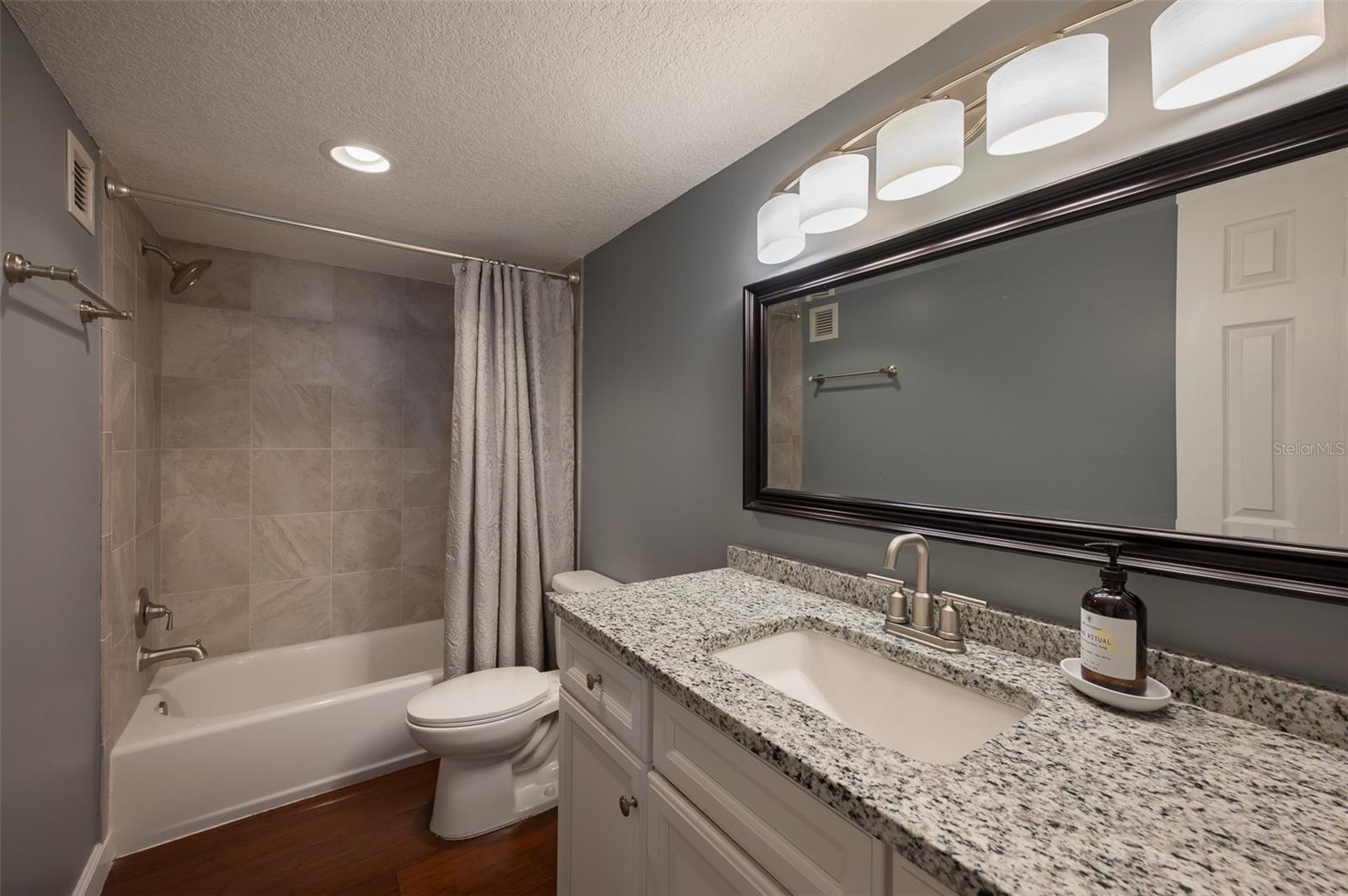 Bathroom with tiled tub and shower, granite vanity, and large framed mirror.
