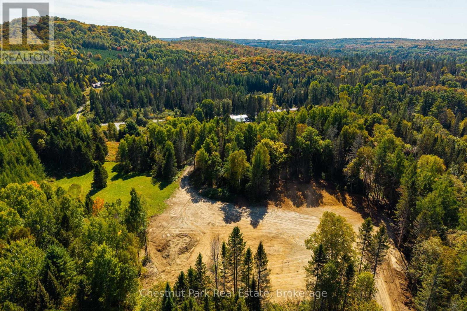 Aerial view of a wooded property with a large cleared area and forested hills beyond.