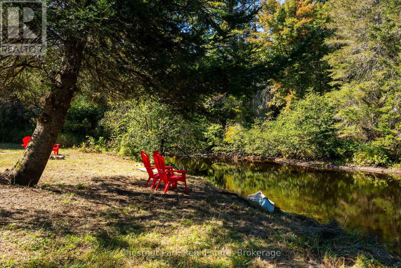 Wooded pond shoreline with red Adirondack chairs and a canoe at the water’s edge.