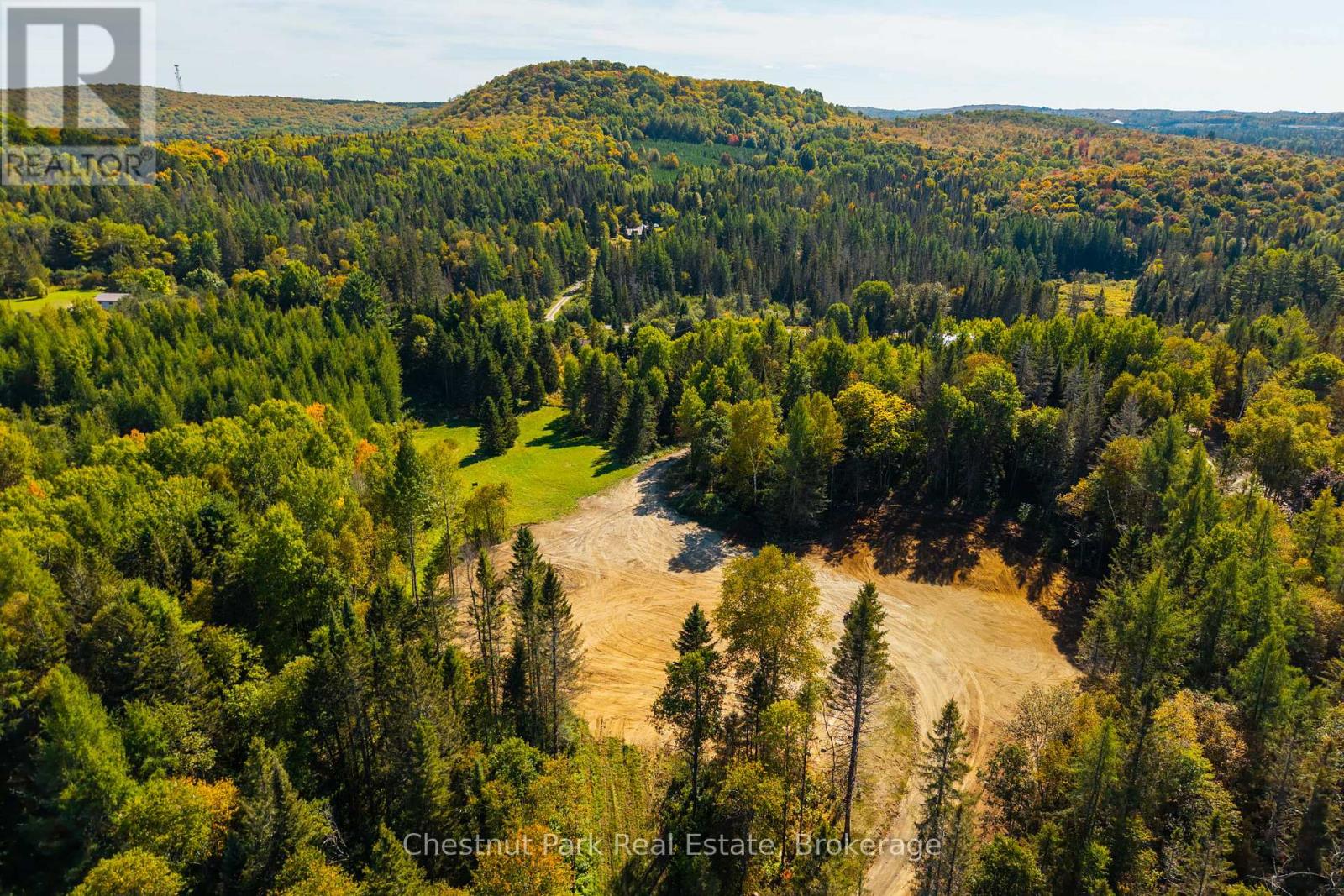Aerial view of a forested property with a broad cleared area and winding access road.