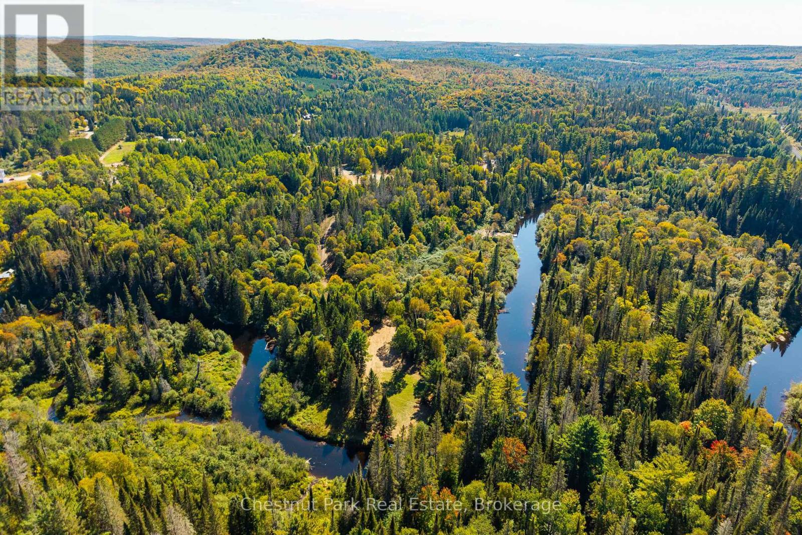 Aerial view of a winding river through autumn forest and scattered clearings.