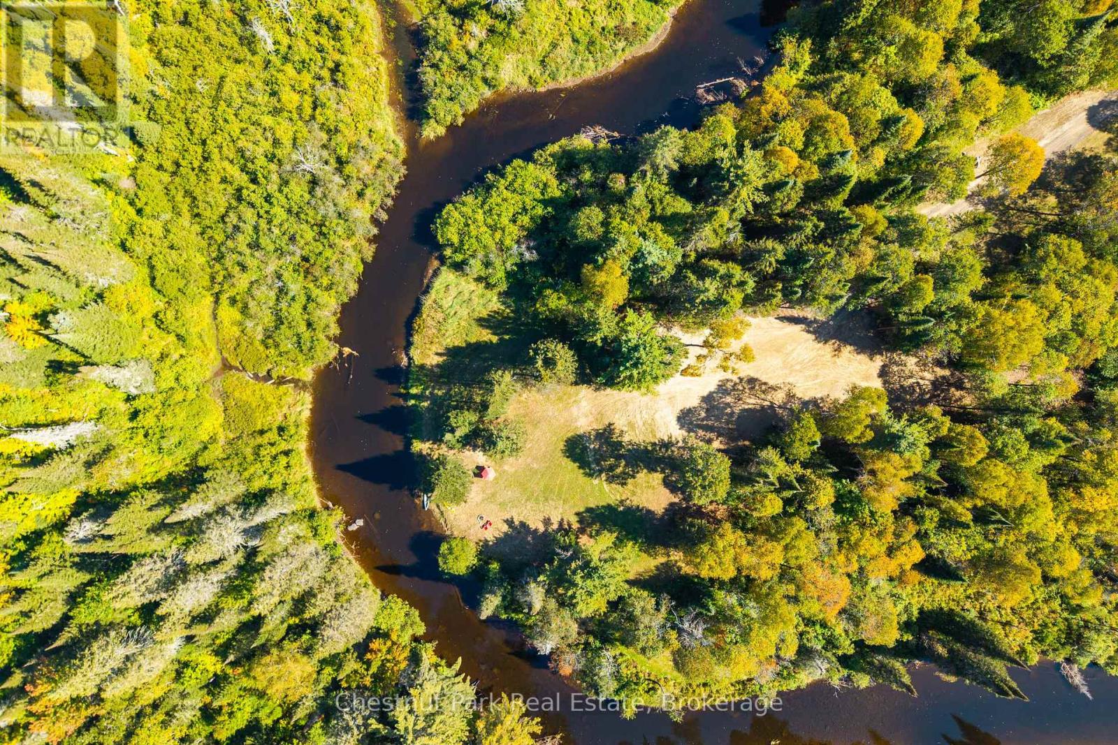 Aerial view of a wooded riverfront property with a grassy clearing and winding river.