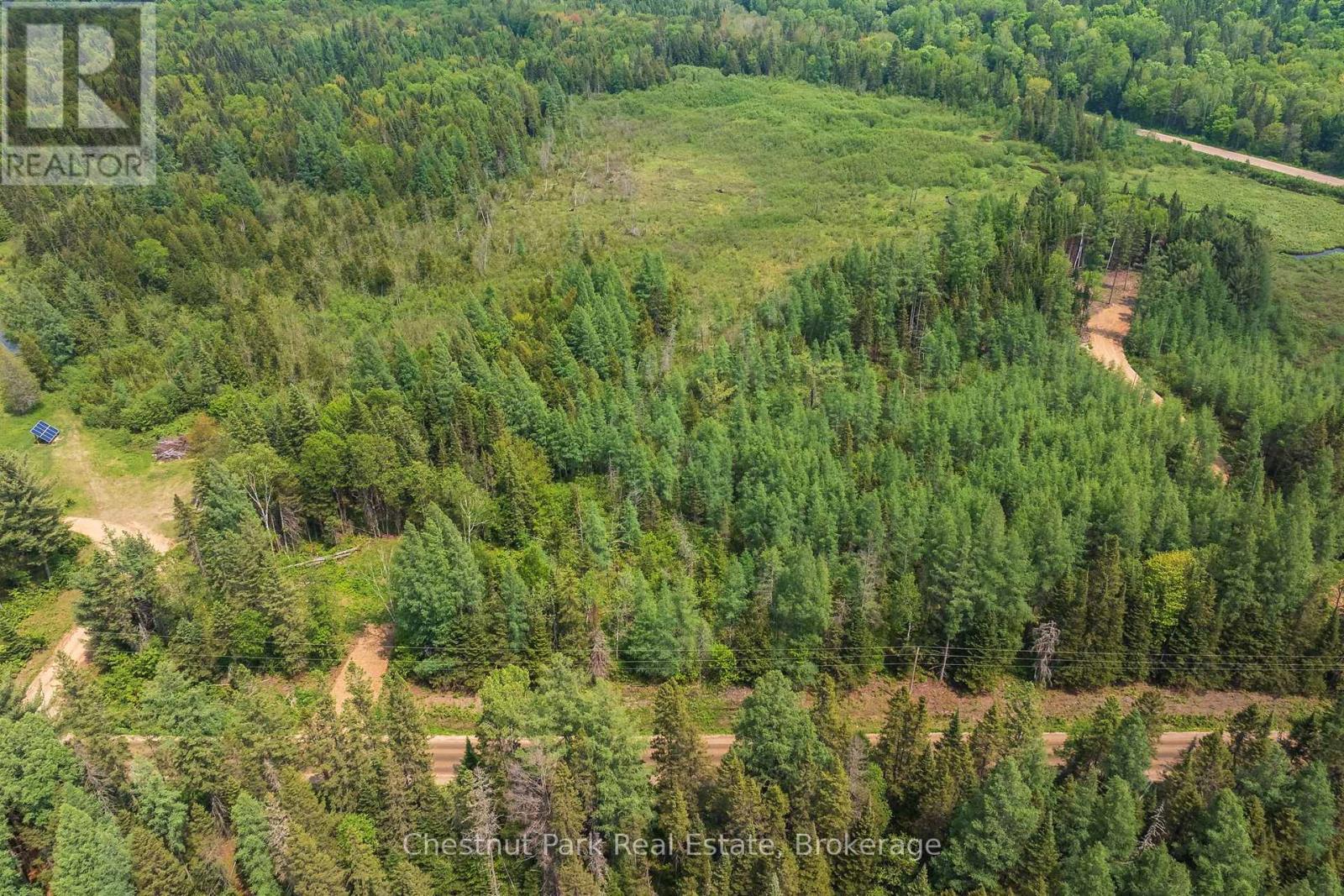 Aerial view of a wooded property with a broad clearing and dirt access tracks.