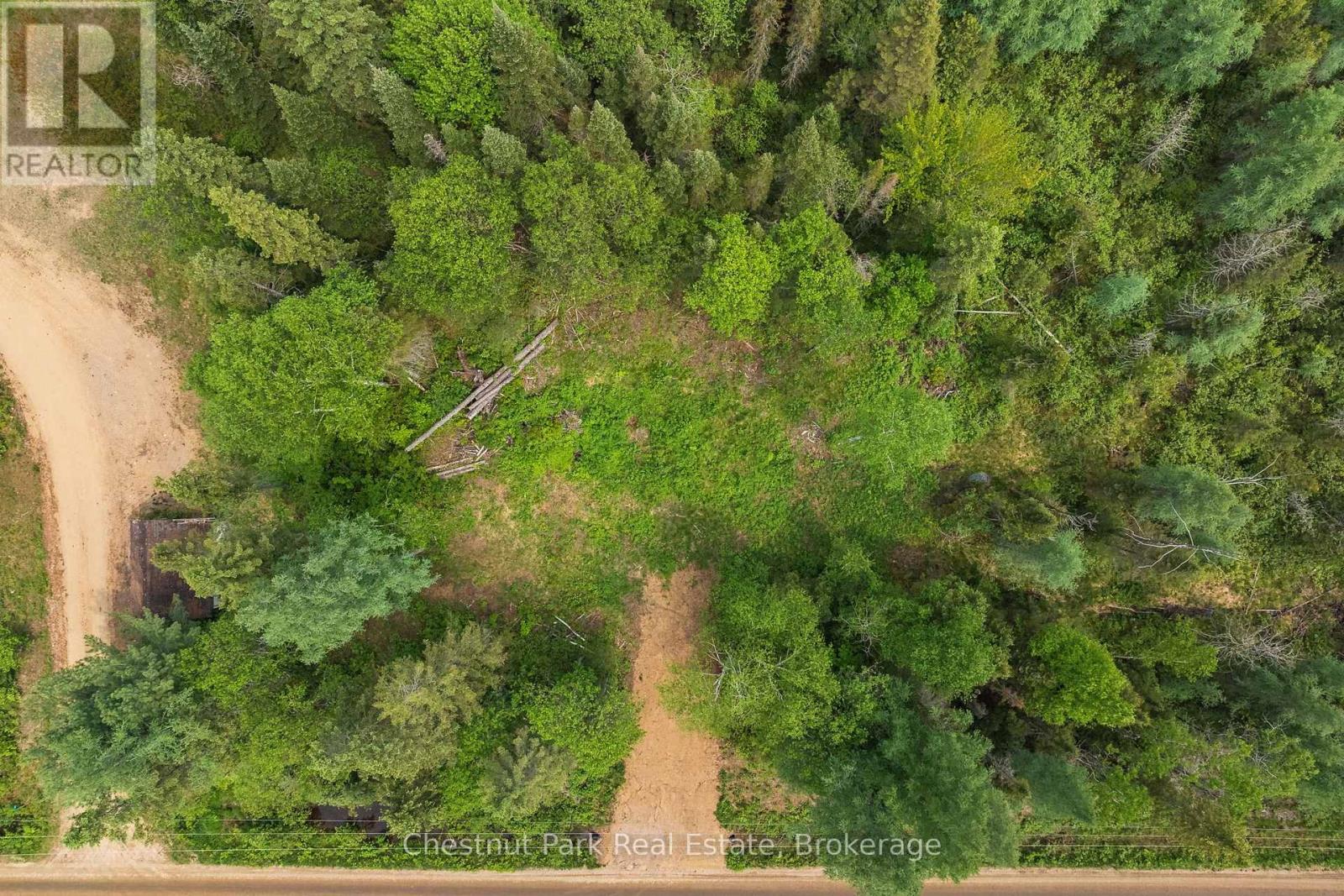 Aerial view of a wooded vacant lot with a clearing, dirt access tracks, and road frontage.