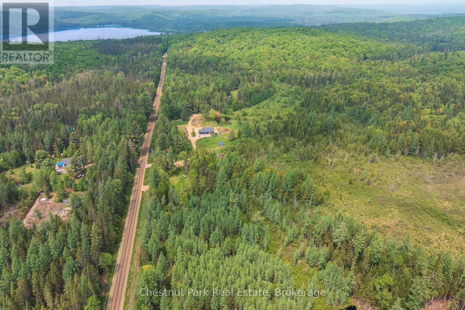 Aerial view of a forested property with a road, a clearing with buildings, and a distant lake.