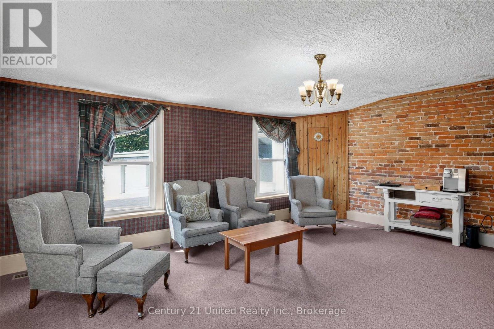 Living room with gray armchairs, plaid wallpaper, and an exposed brick wall.