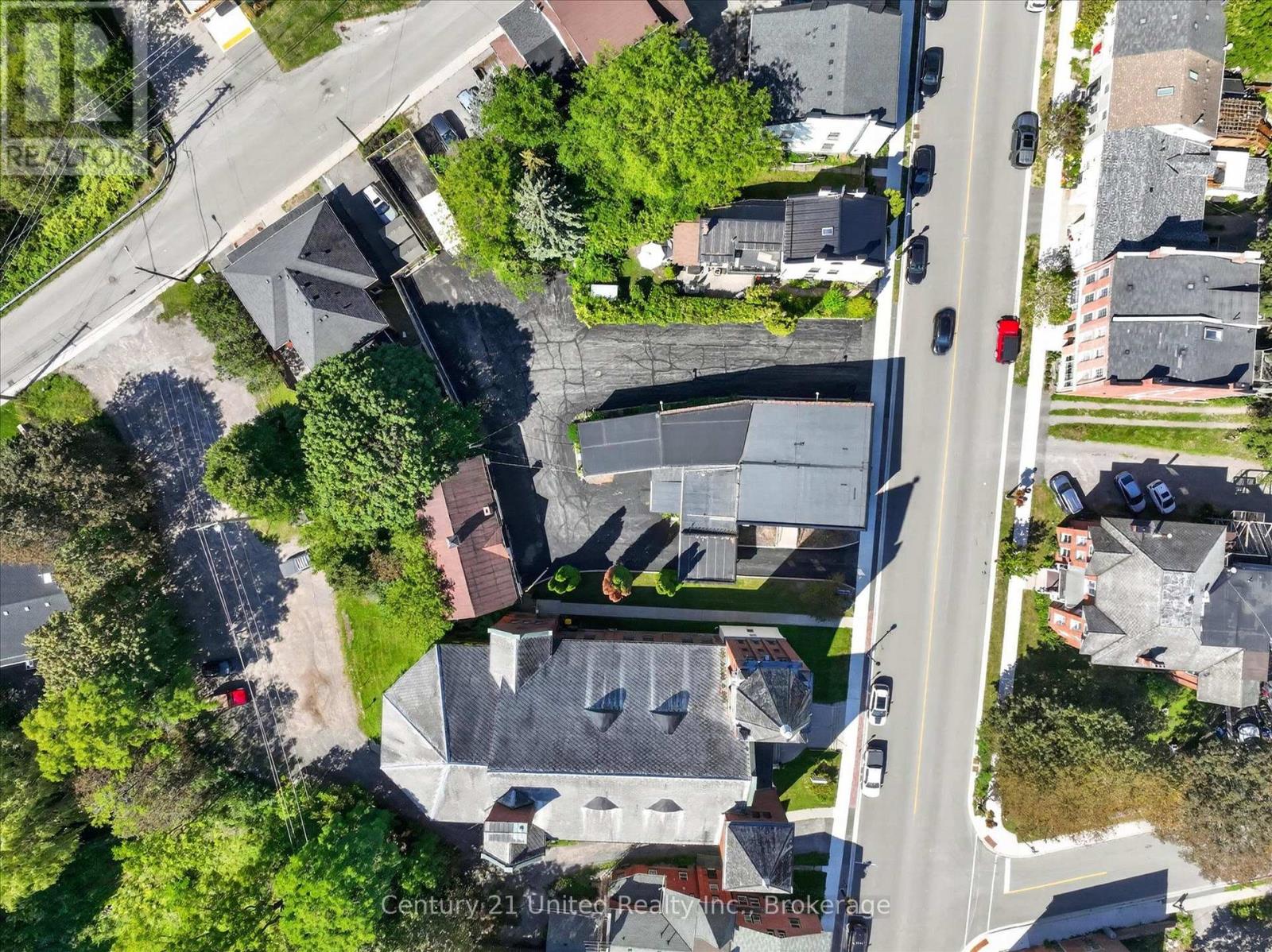 Aerial view of a low-rise building and paved lot beside a road, surrounded by trees and neighboring buildings.