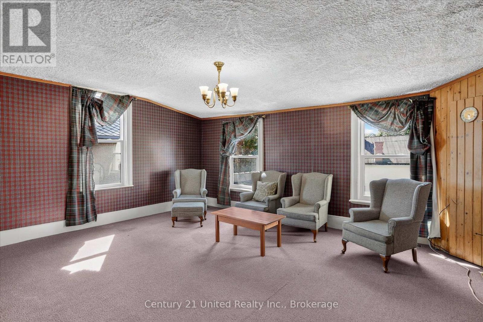 Living room with plaid wallpaper, gray armchairs, mauve carpet, and a wood-paneled wall.