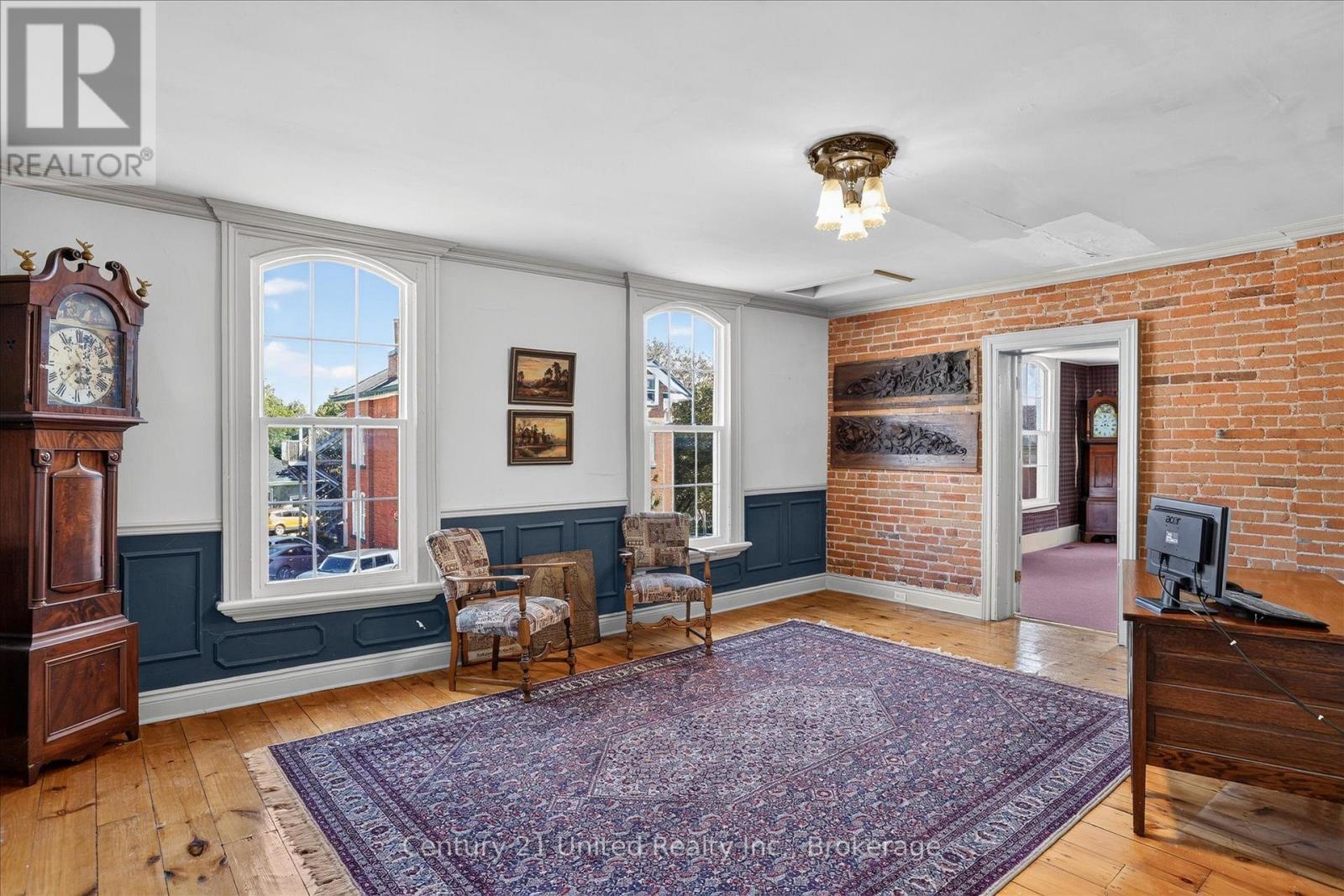 Historic living room with exposed brick, arched windows, dark blue wainscoting, and a large patterned rug.