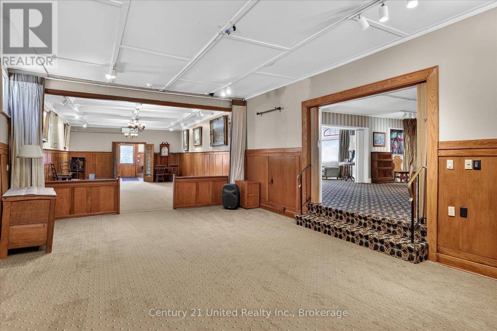 Spacious carpeted room with wood paneling and a wide doorway to an adjoining room.