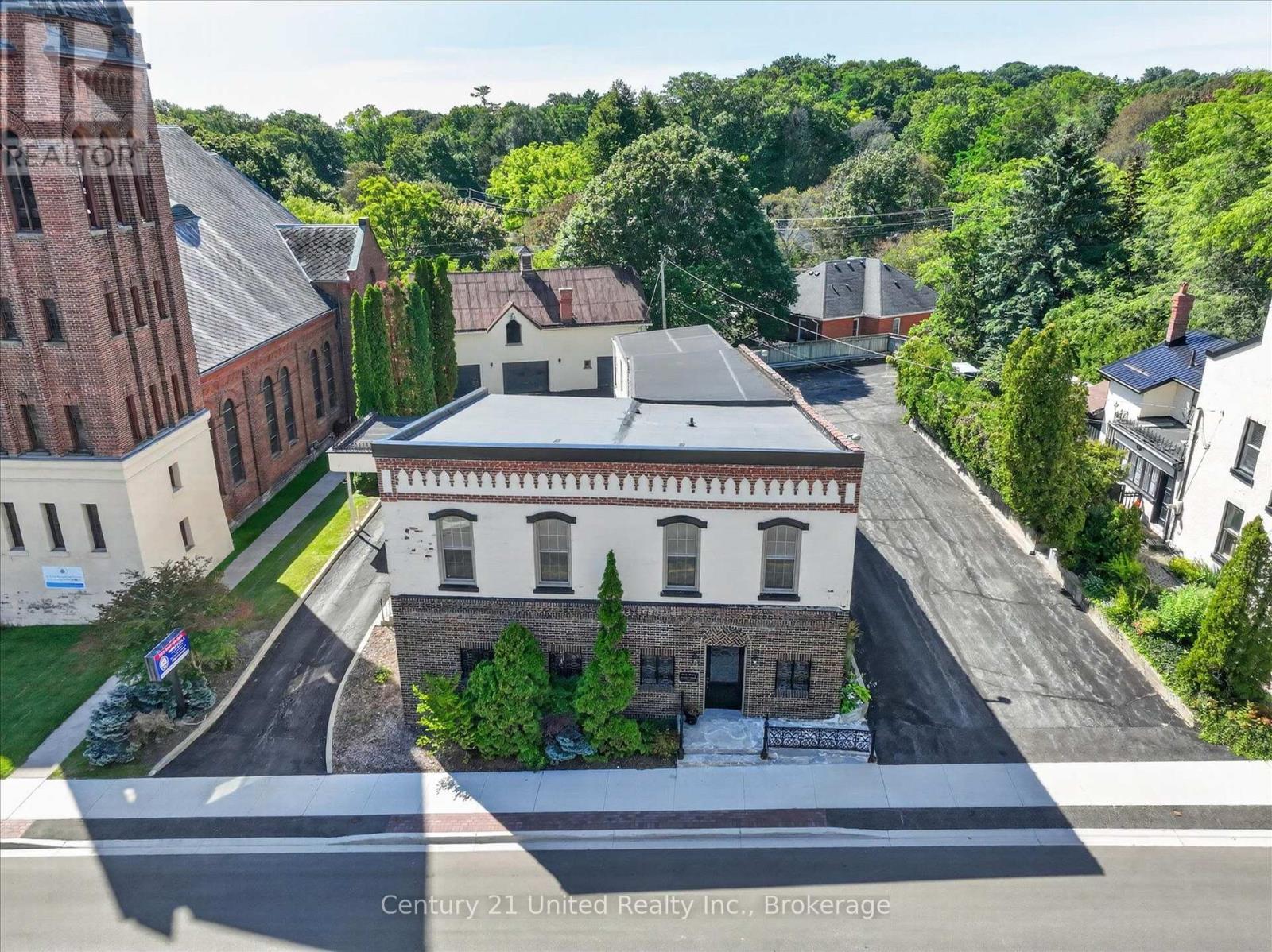 Two-story brick-and-white building with a flat roof, landscaped frontage, and neighboring downtown buildings.