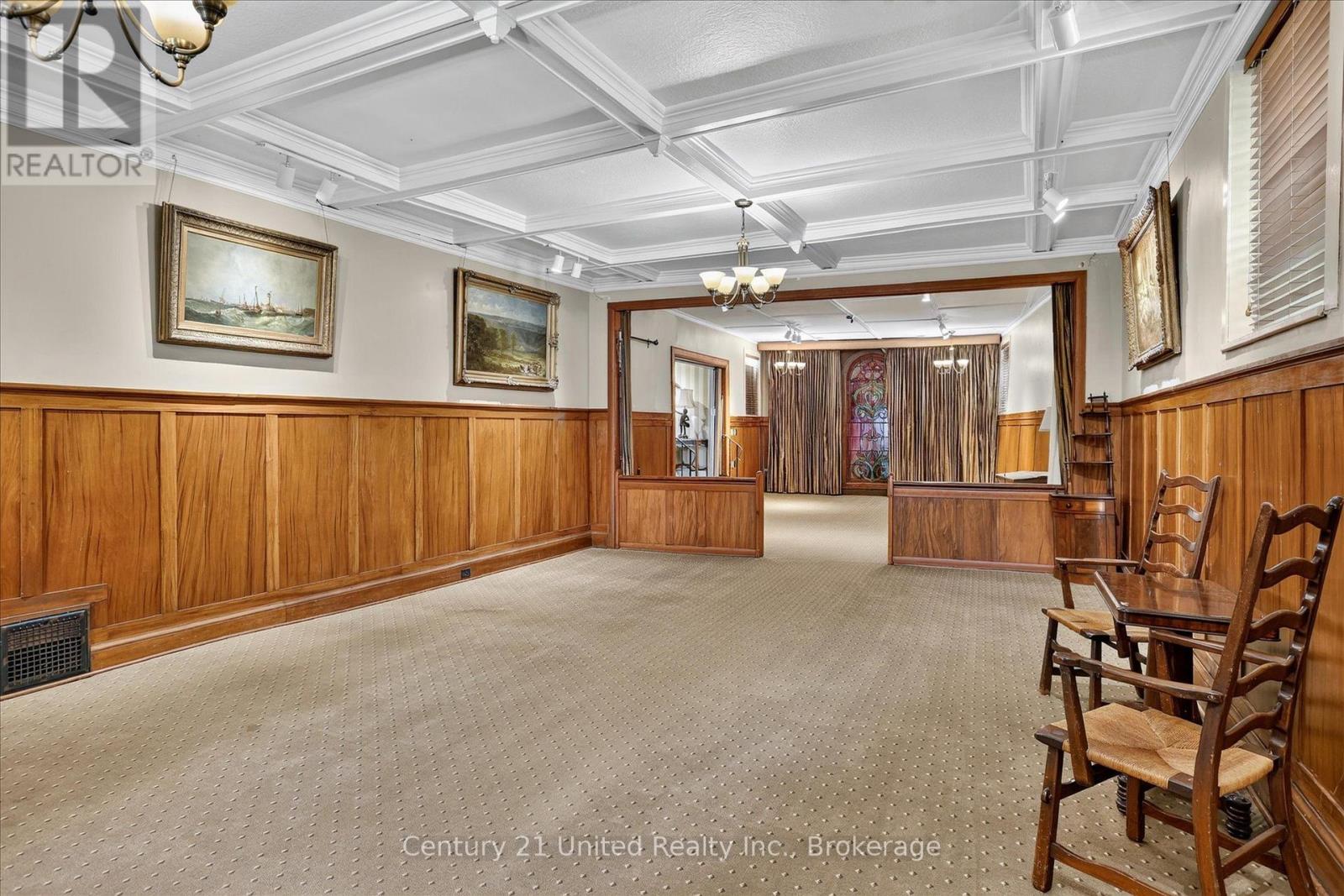 Long wood-paneled room with a coffered ceiling, patterned carpet, and wooden chairs.