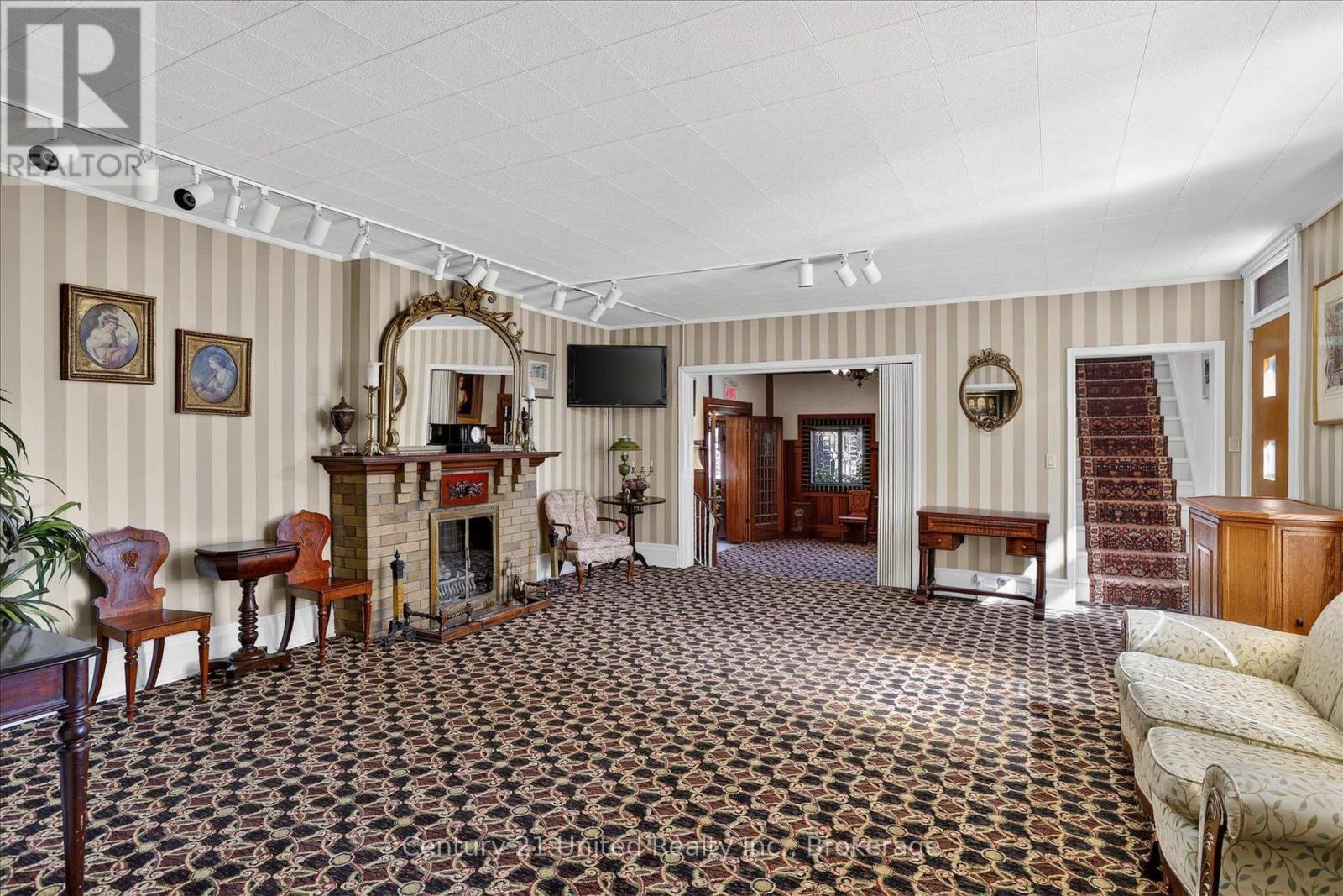 Furnished living room with a brick fireplace, ornate mirror, striped walls, and patterned carpet.