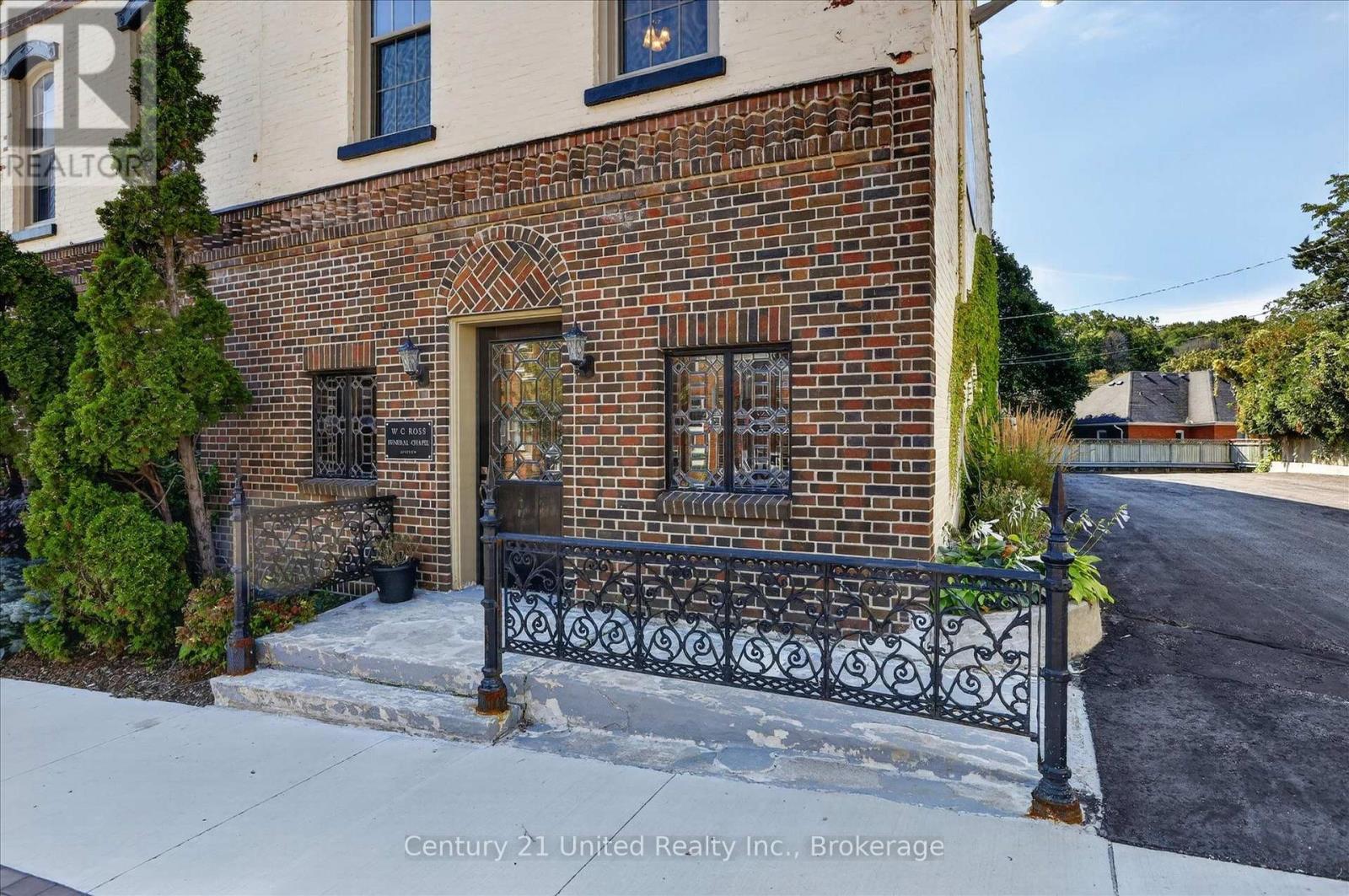 Brick building entrance with an arched doorway, decorative windows, and ornate iron railings.