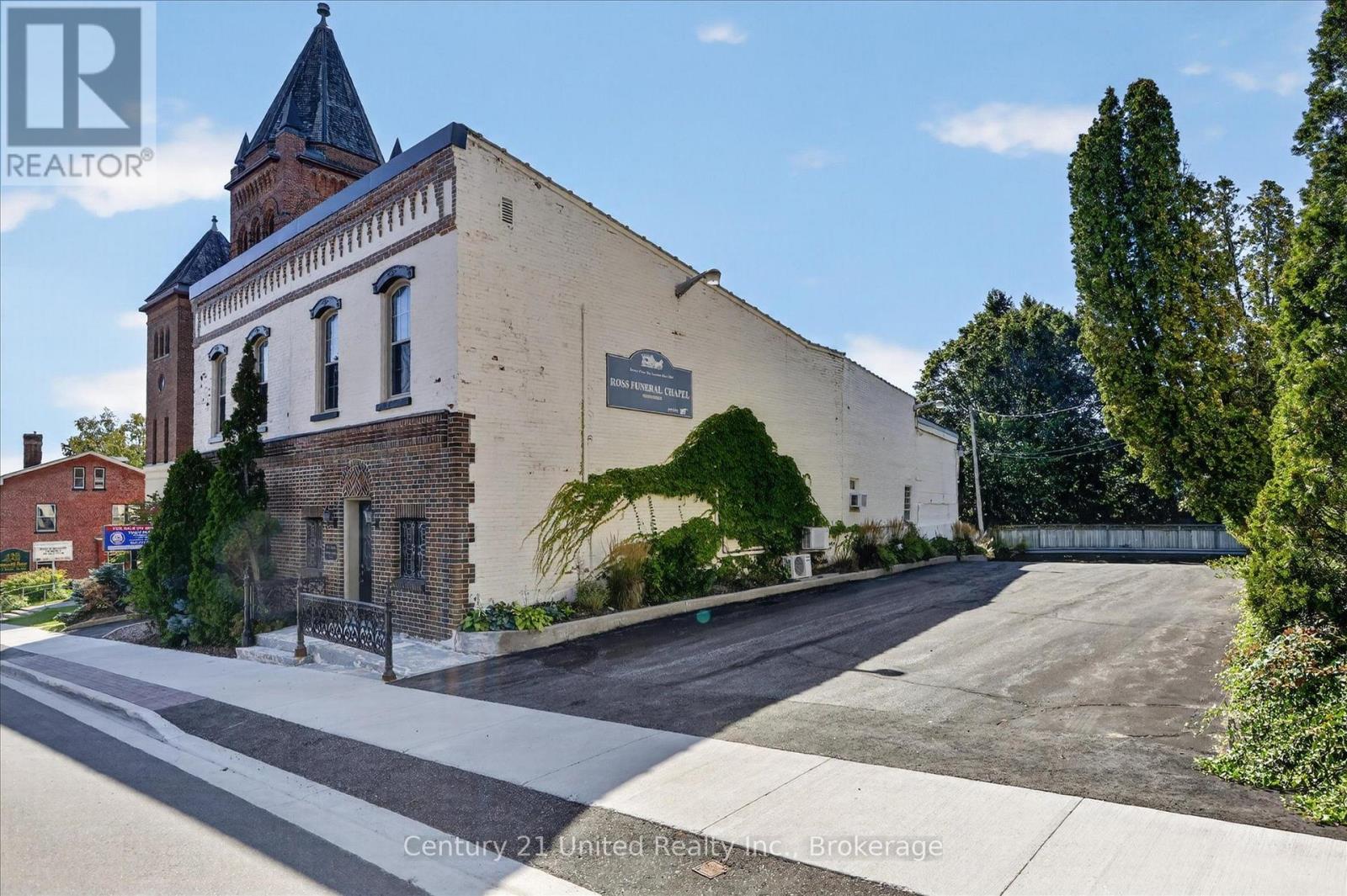 Historic chapel exterior with a tall peaked tower, ivy-covered wall, and paved parking area.