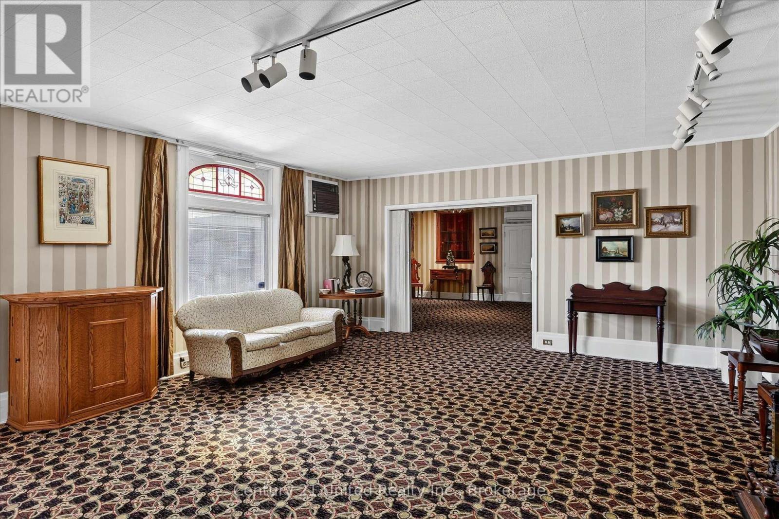 Furnished living room with striped walls, patterned carpet, cream sofa, and a wide doorway to an adjoining room.