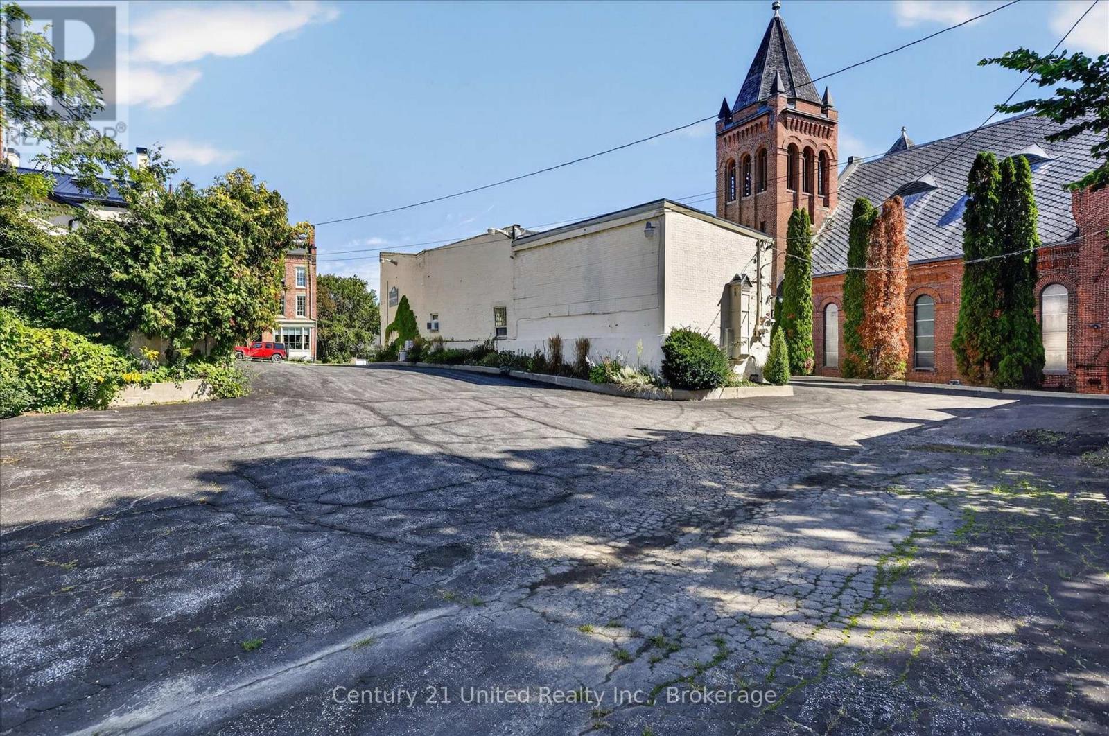 Paved parking area beside a white building and red-brick church with a tall tower.